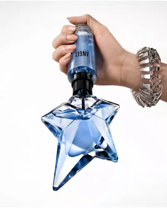A hand holding the classic blue star-shaped Angel Eau de Parfum bottle pointing upwards against a plain white background.