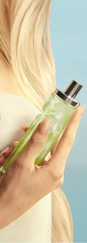 In-hand-Asset des neuen Starlicious Pistachio Praline mit einem Model mit langen blonden Haaren und blauen Augen, das in einem hellgelben Kleid den Pistachio Praline Duftflakon in der Hand hält.